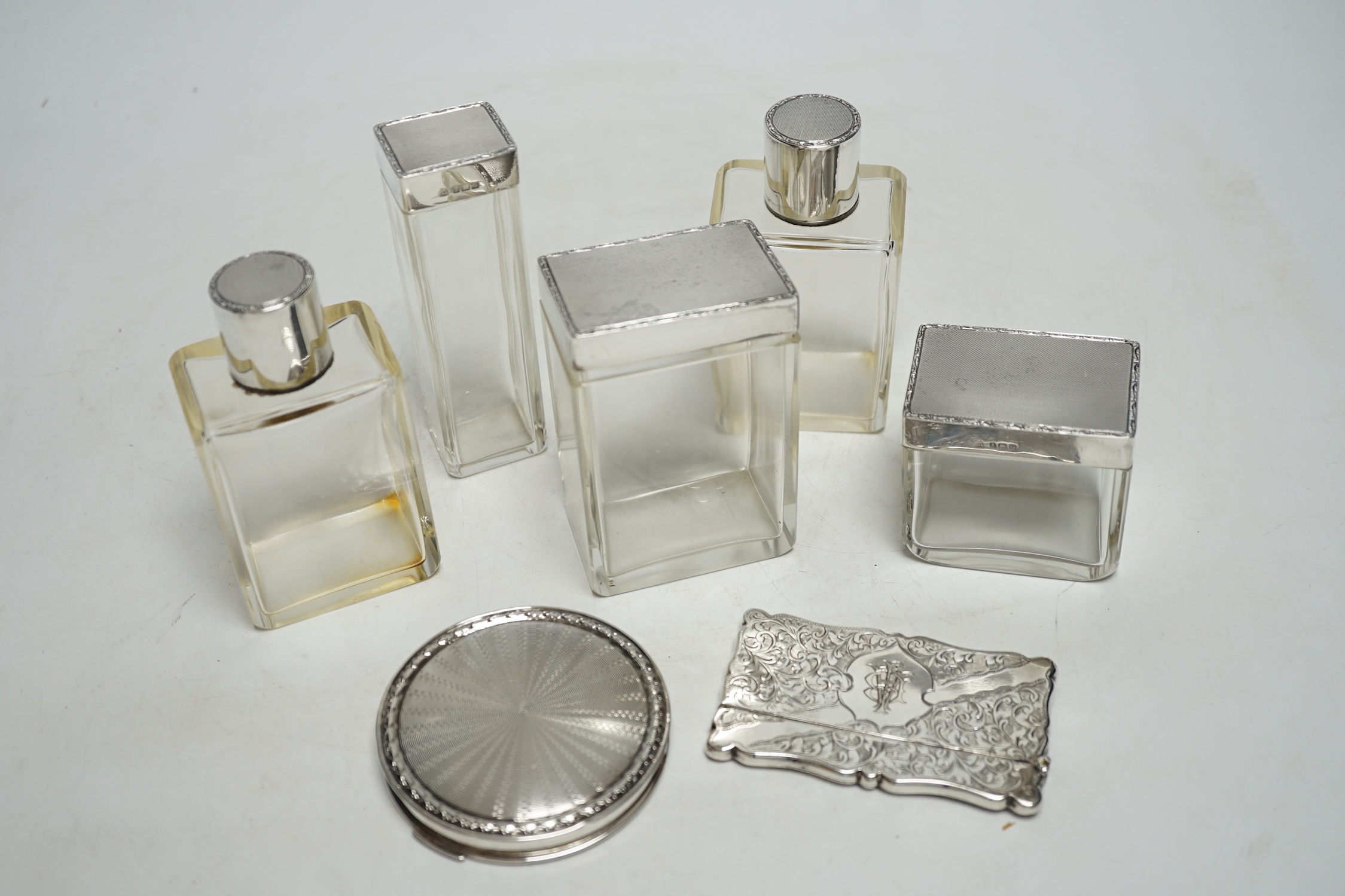 Five assorted silver topped glass toilet jars, a silver compact and an Edwardian engraved silver card case, Birmingham, 1902, 83mm.